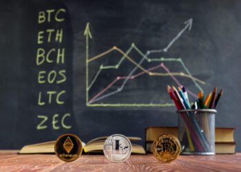 Kurse von Kryptowährungen auf einer Tafel hinter einem Schreibtisch mit Stiften und Krypto-Coins.